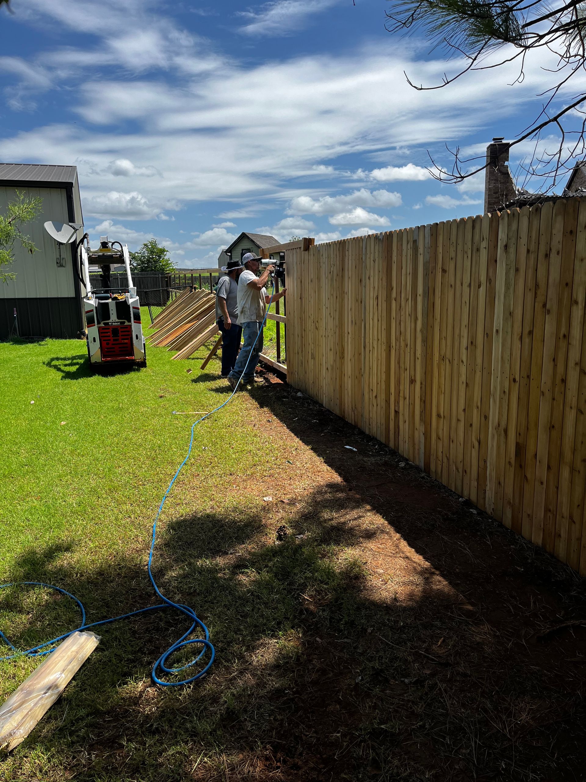 Two workers building a wooden fence in a sunny backyard.