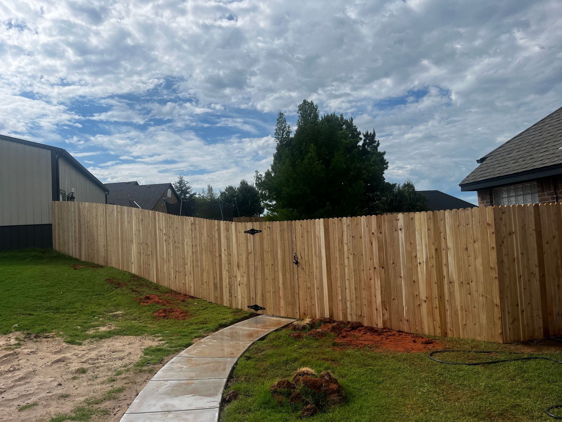 Wooden fence along a curved concrete path, with green grass and cloudy sky.