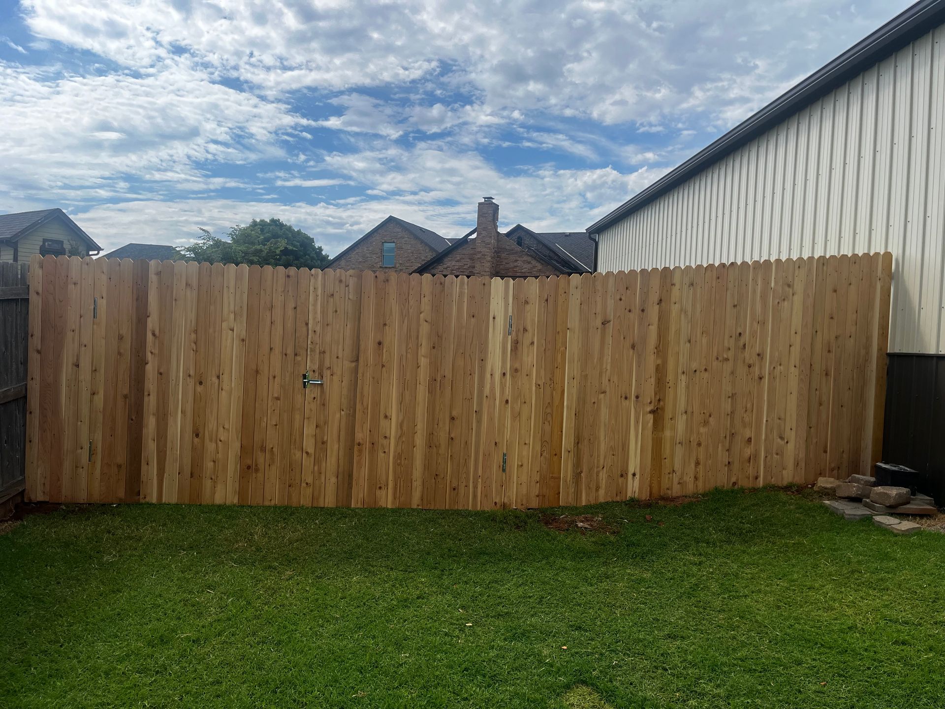 Wooden fence in a backyard with green grass and a cloudy sky.