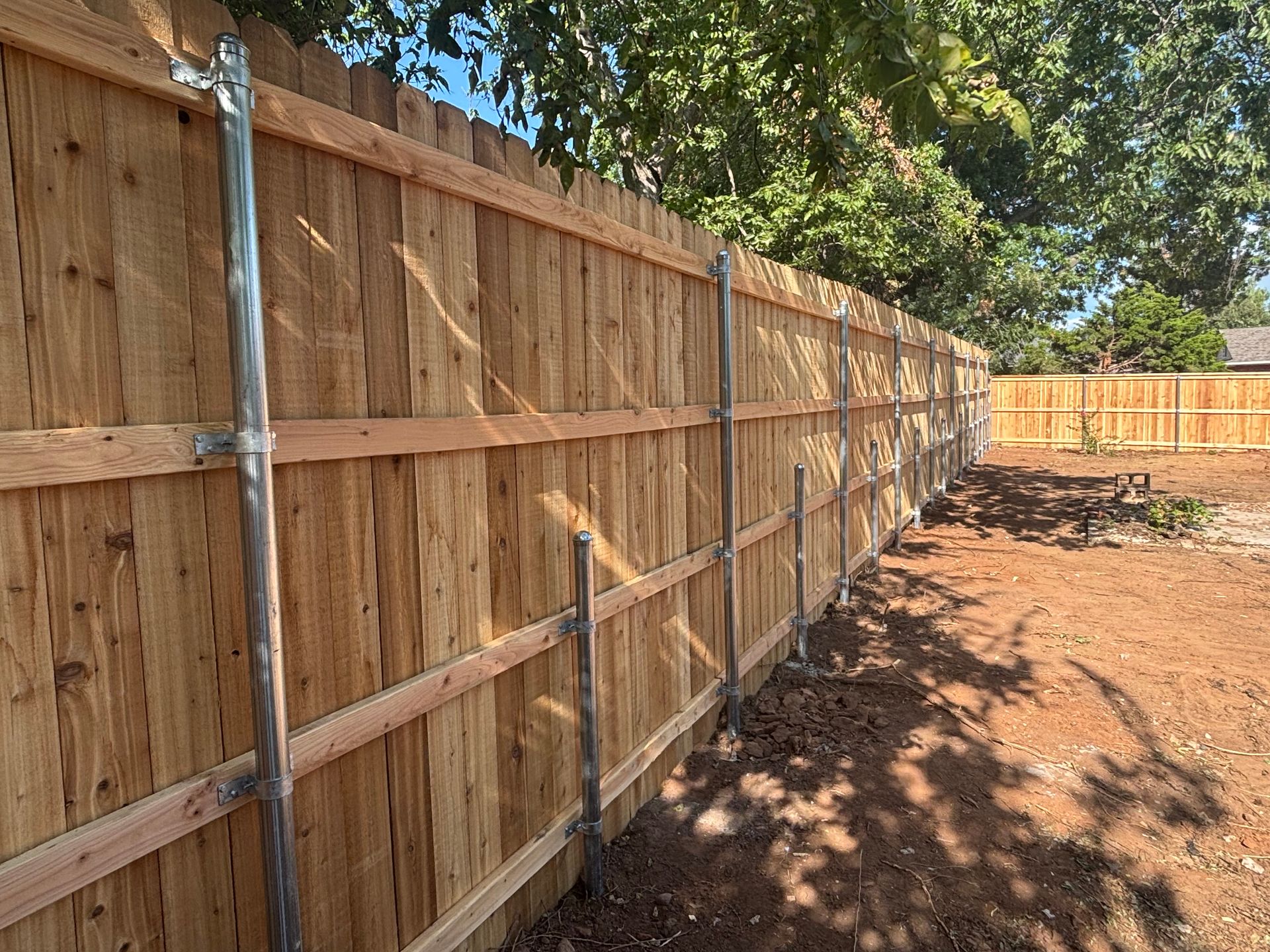 Wooden fence with metal posts in a backyard setting.