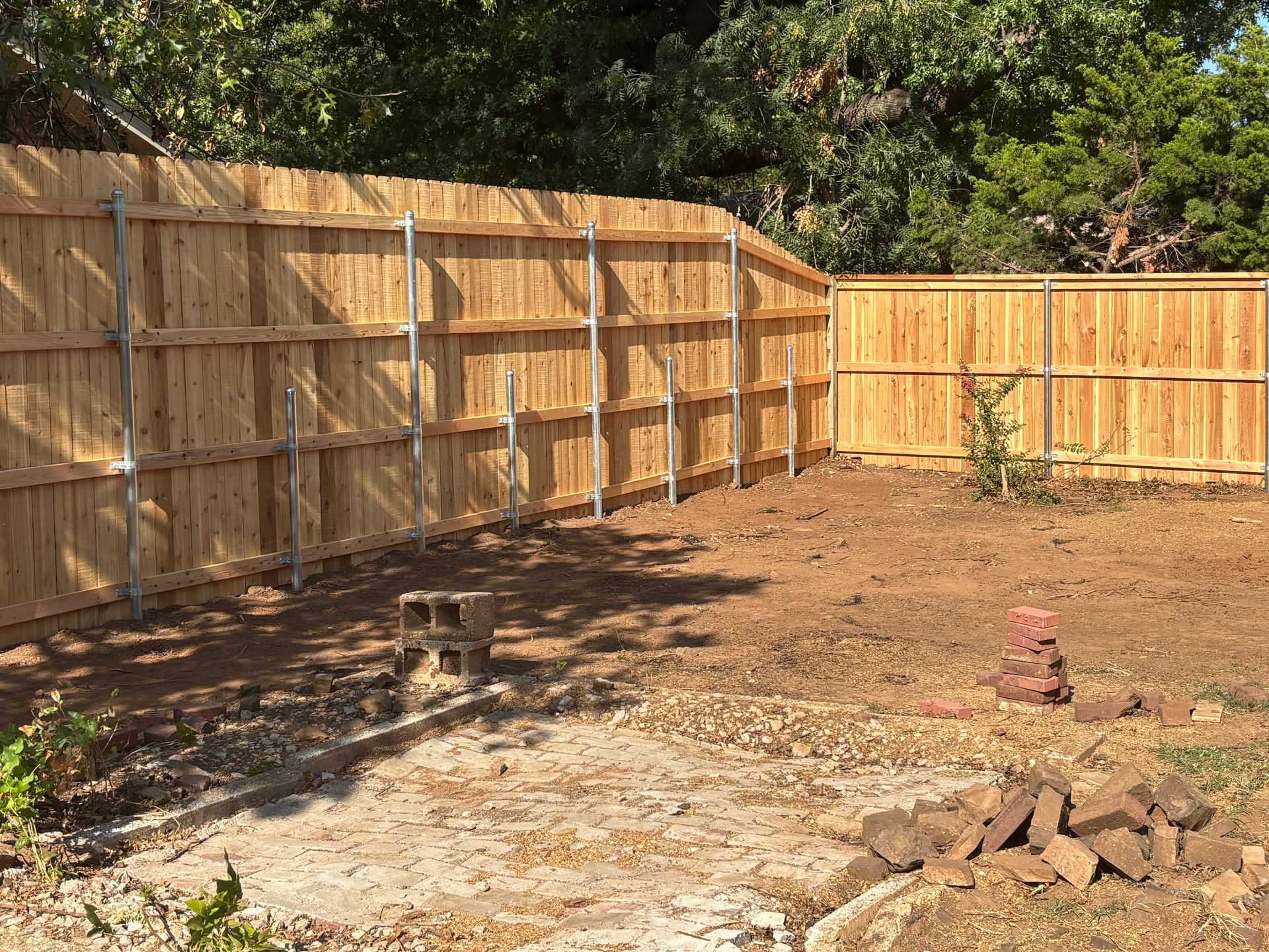 Wooden fence in a backyard, with dirt ground and trees in the background.