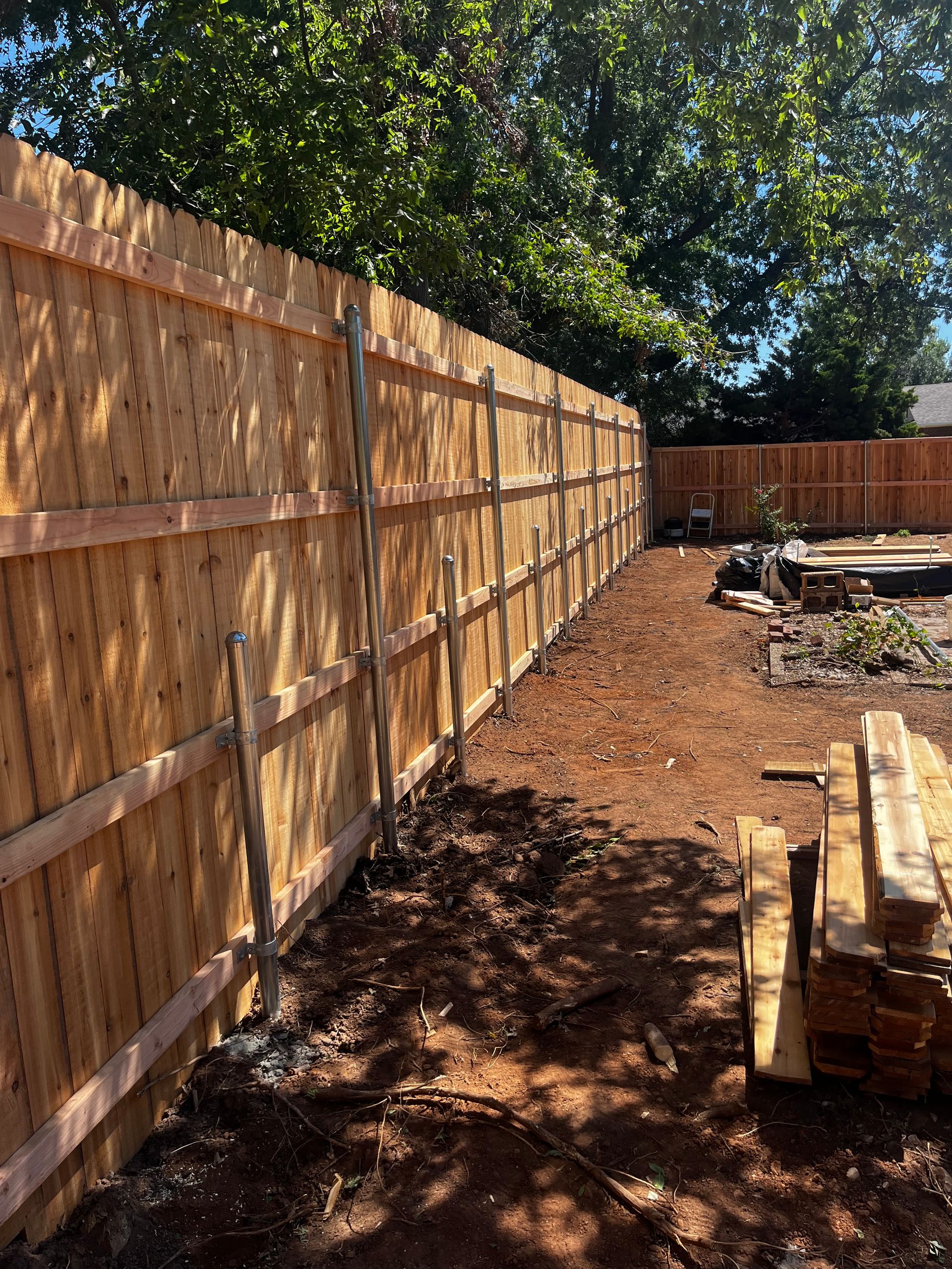 Wooden fence in backyard with brown planks, and metal posts.