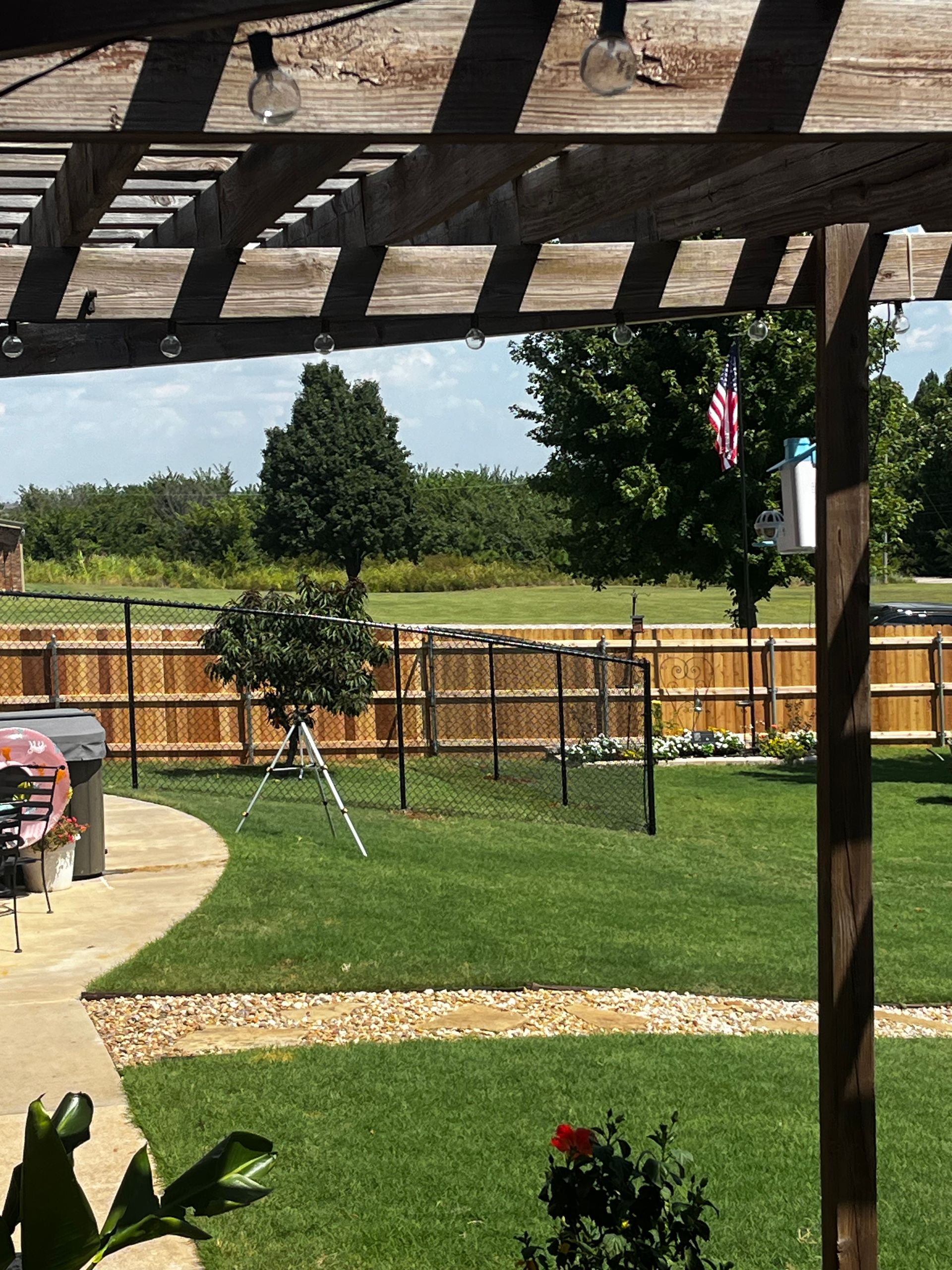 Lawn with a wooden pergola, fence, and trees.