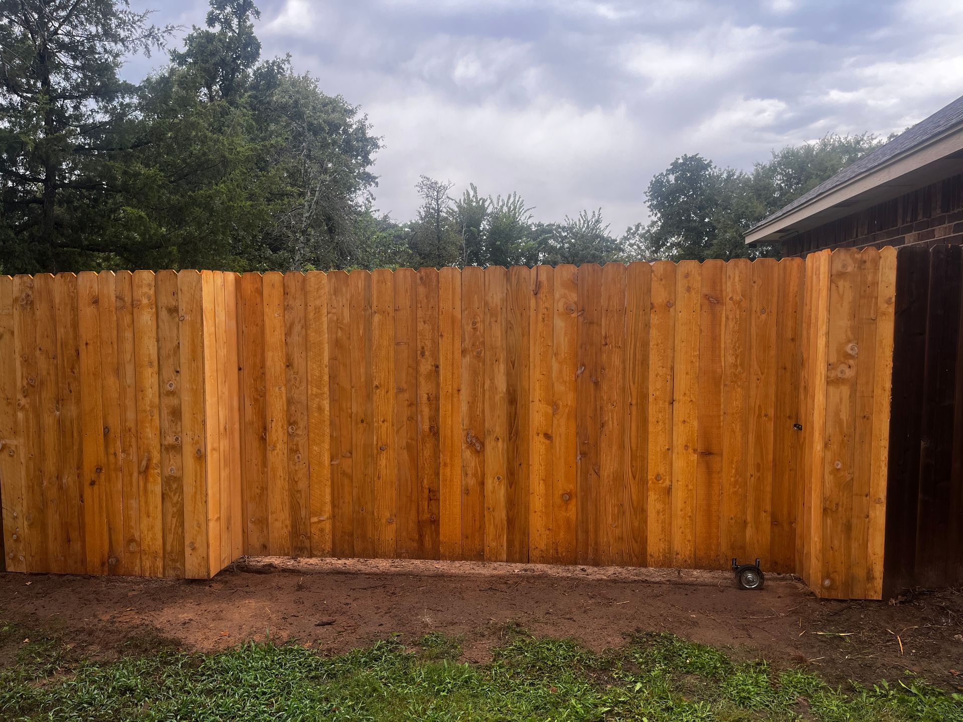 Wooden fence with natural wood grain, in a yard with grass and trees in the background.