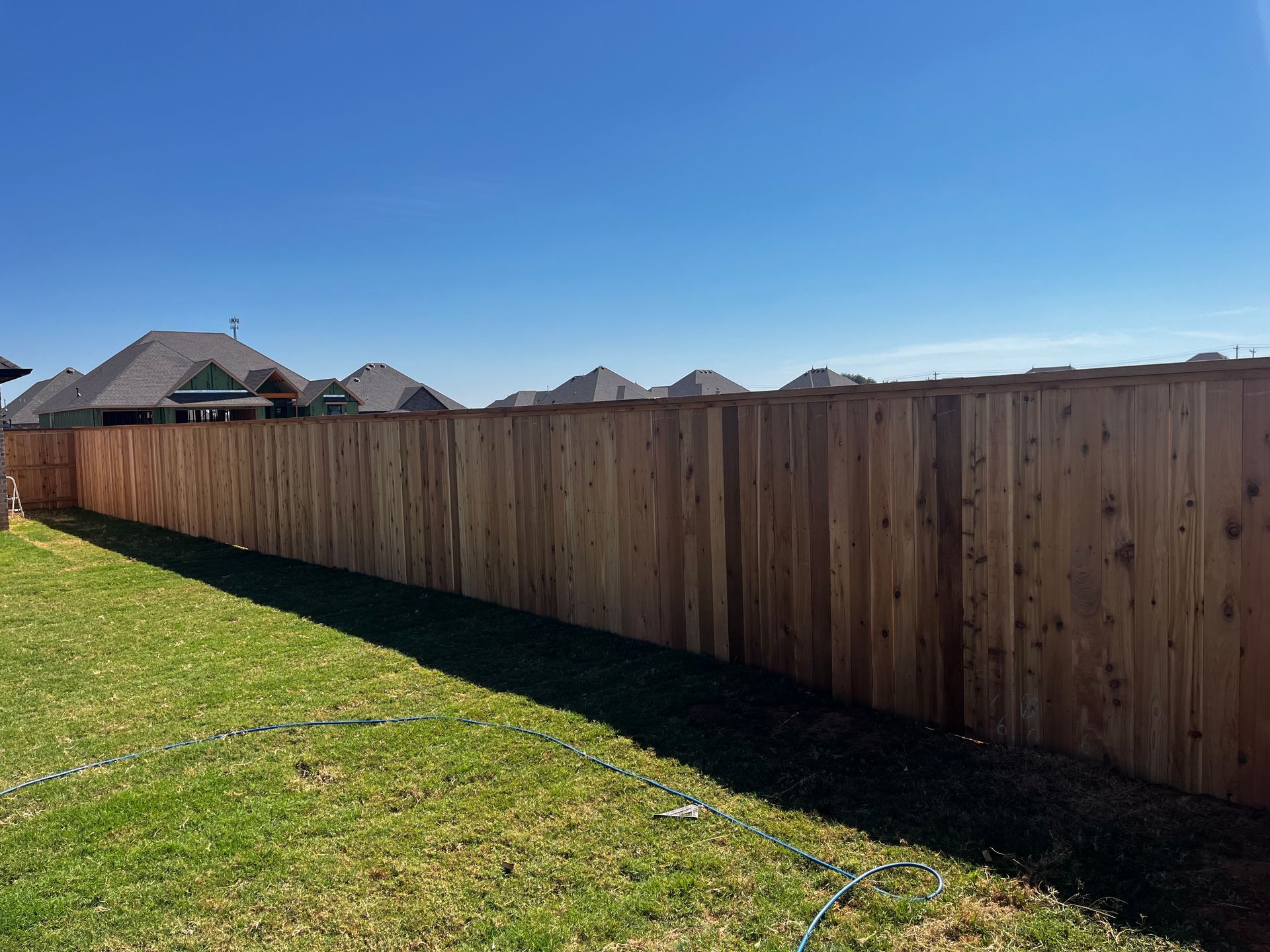 Wooden fence in a backyard on a sunny day with green grass and blue sky.