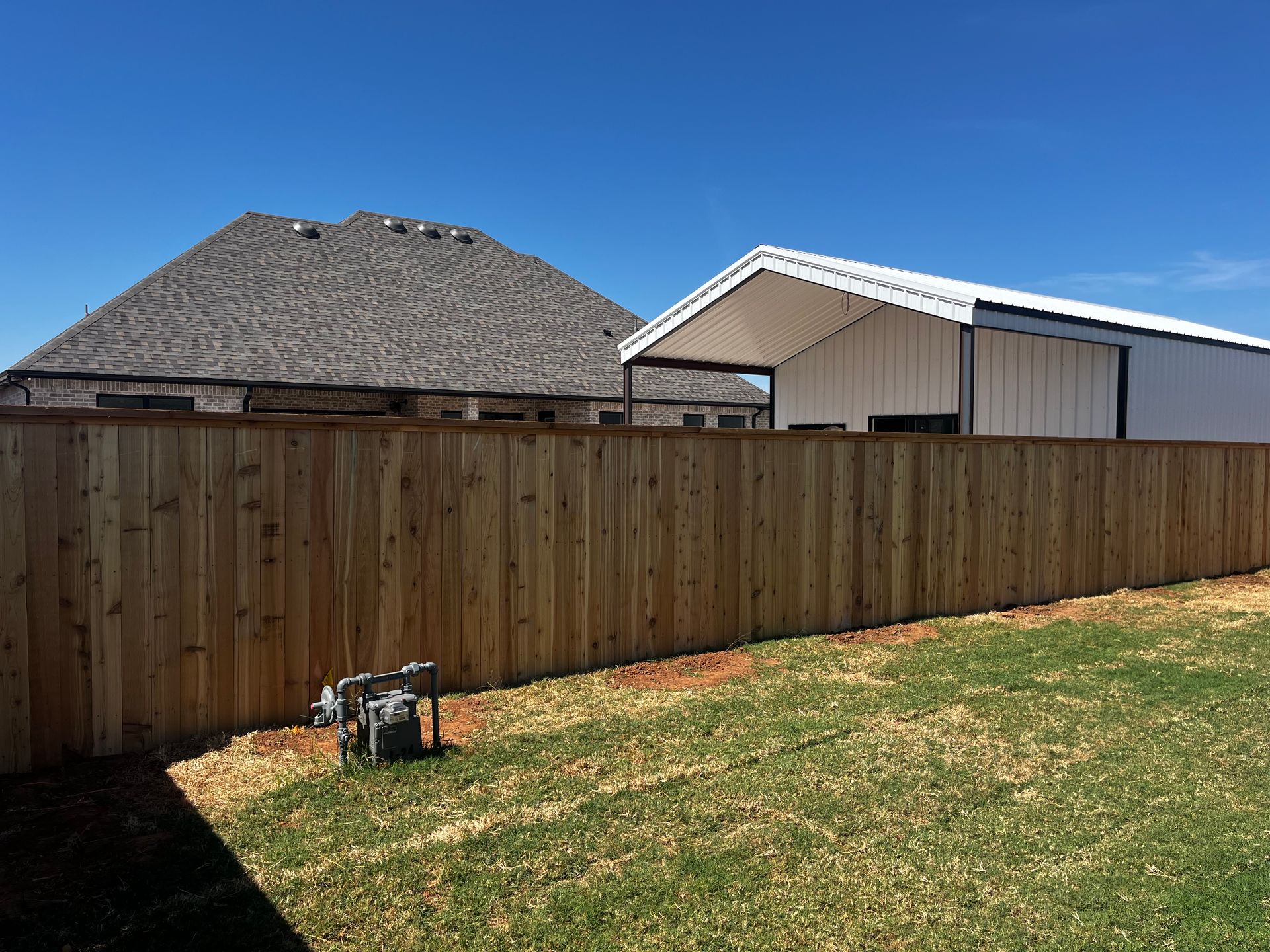 Wooden fence encloses a yard with a house and barn on a sunny day.