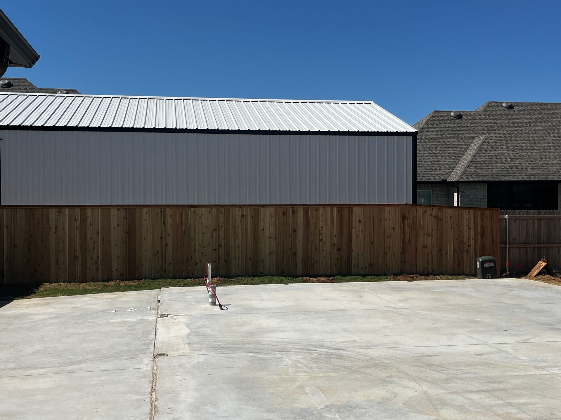 A white metal building with a black trim, behind a brown wooden fence, in a backyard.