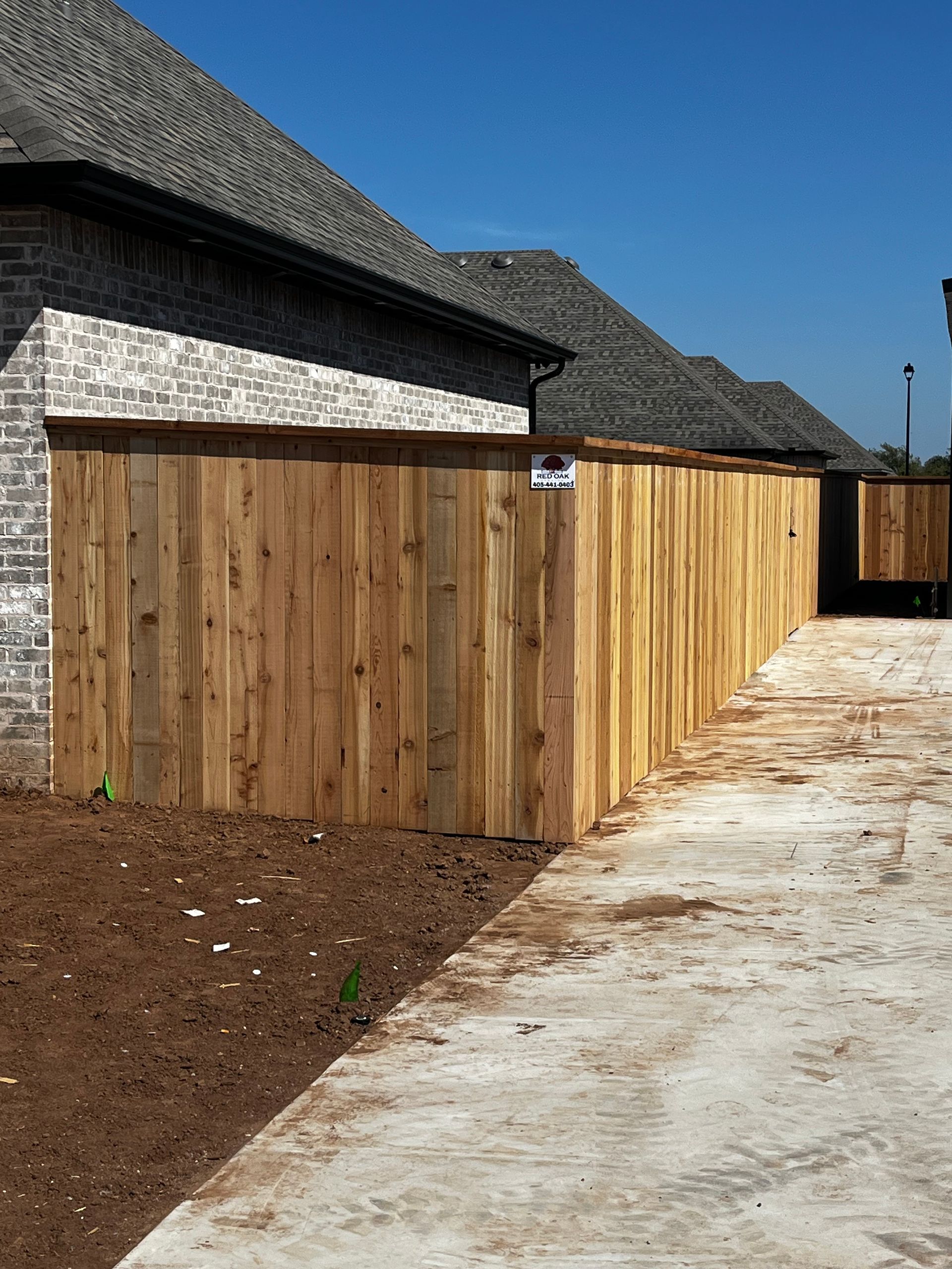 Wooden fence beside a brick building and a concrete walkway.