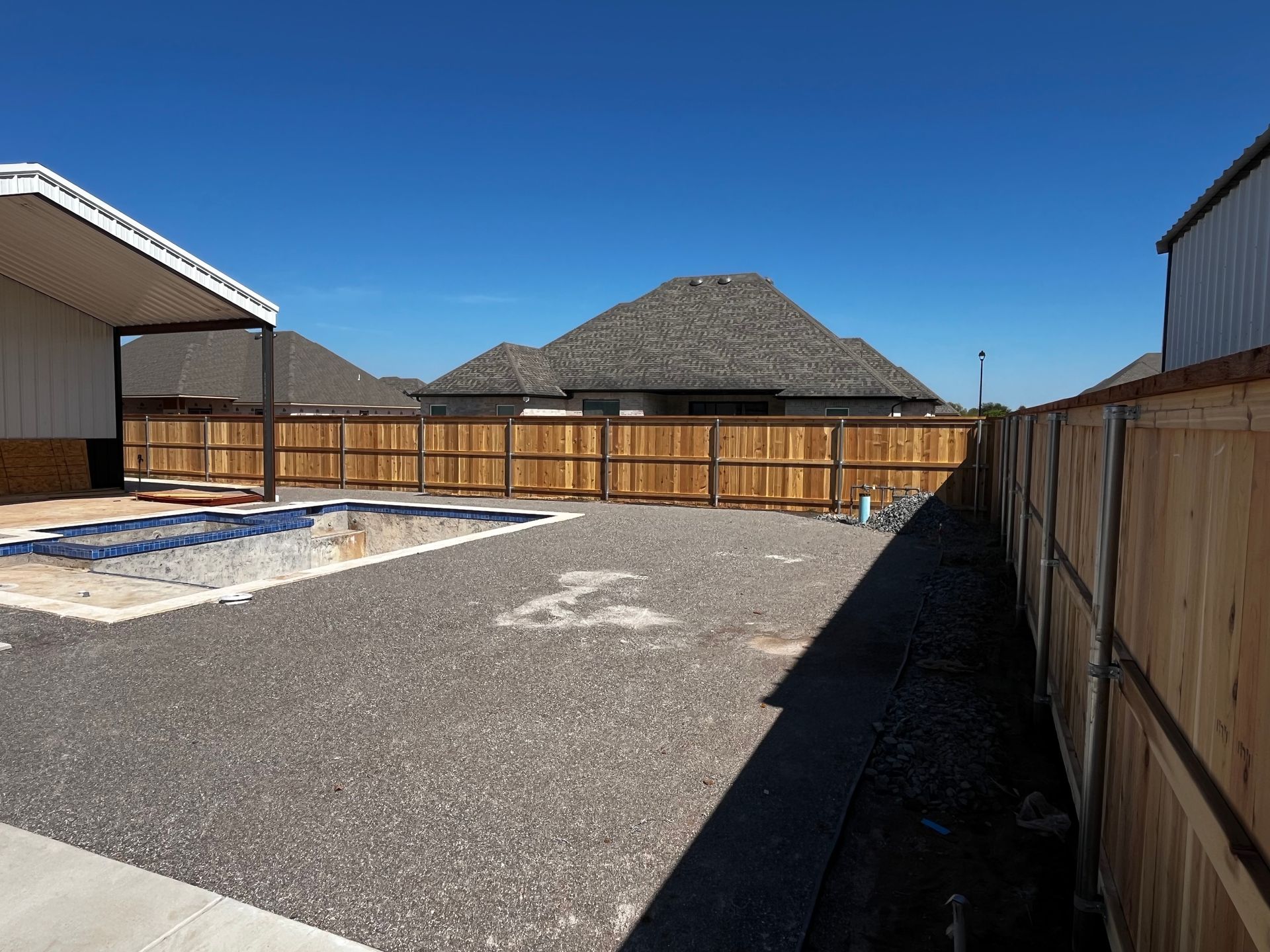Backyard with a wooden fence, gravel ground, and a pool under construction.
