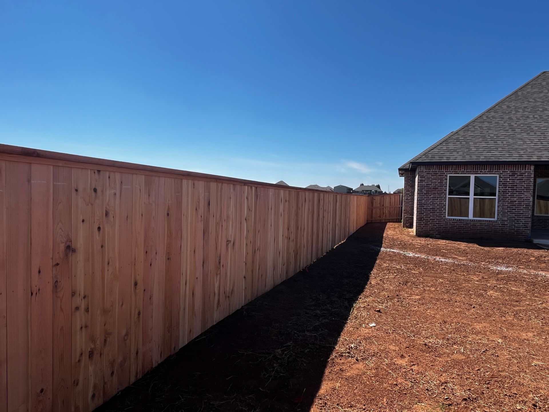A wooden fence lines a yard next to a house on a sunny day.