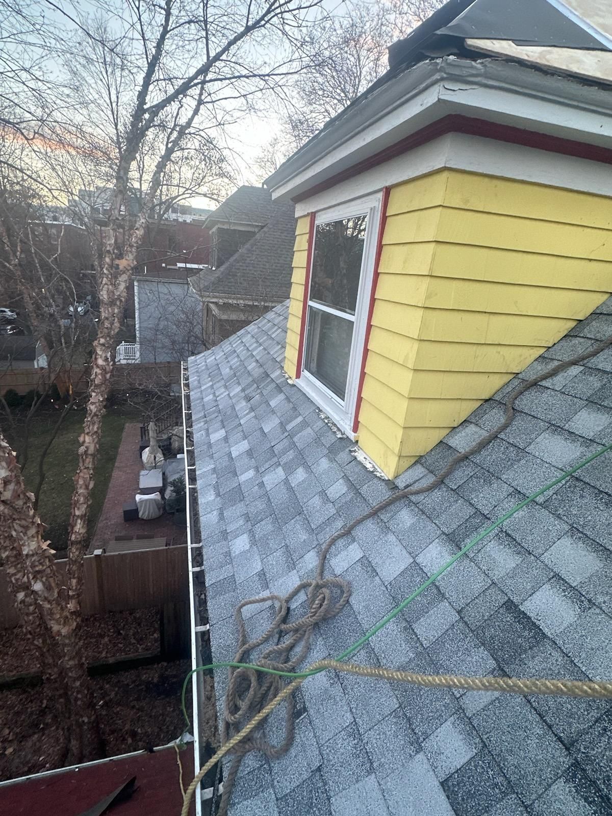 The roof of a house with a yellow siding and a window.