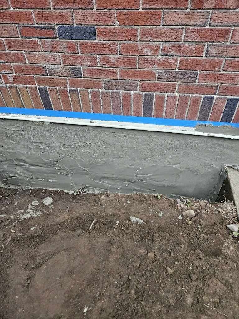 A brick wall with concrete being poured on it.