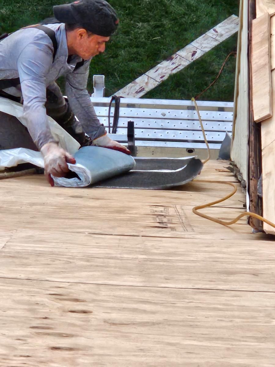 A man is laying a piece of roofing material on a wooden floor.