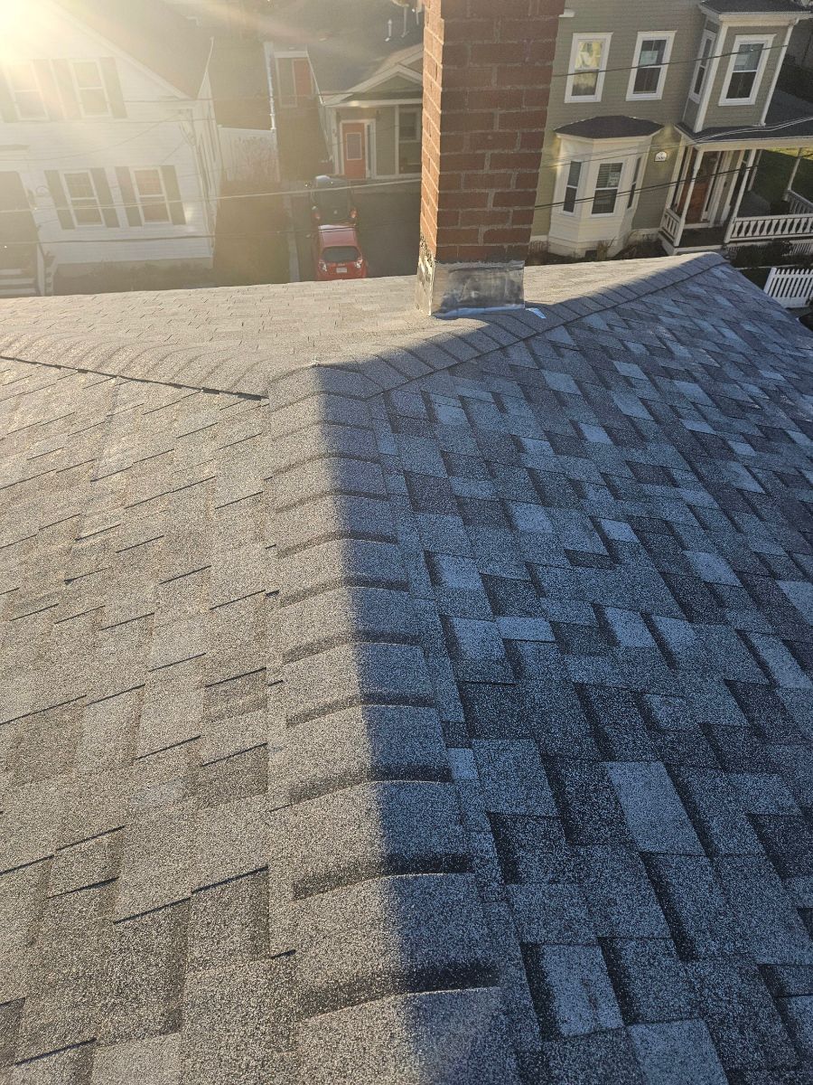 A close up of a roof with a chimney and houses in the background.