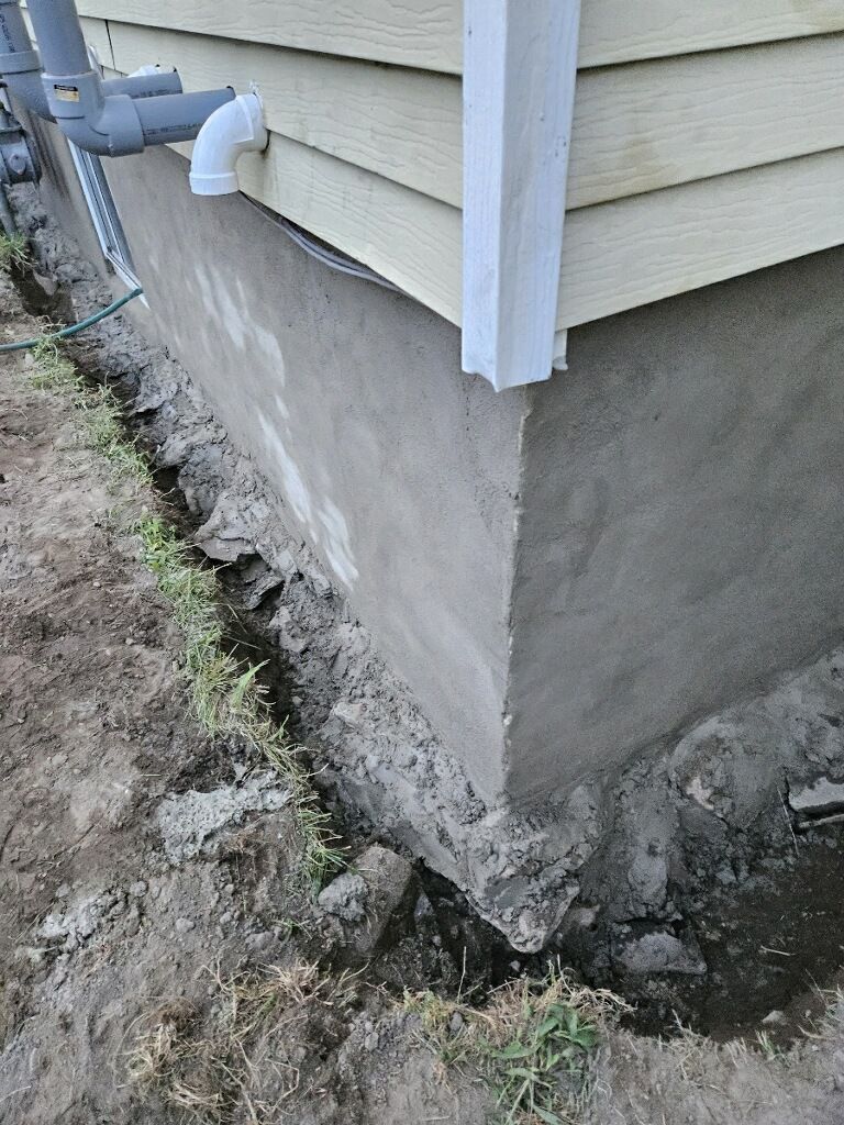 The corner of a house with a hole in the ground next to it.