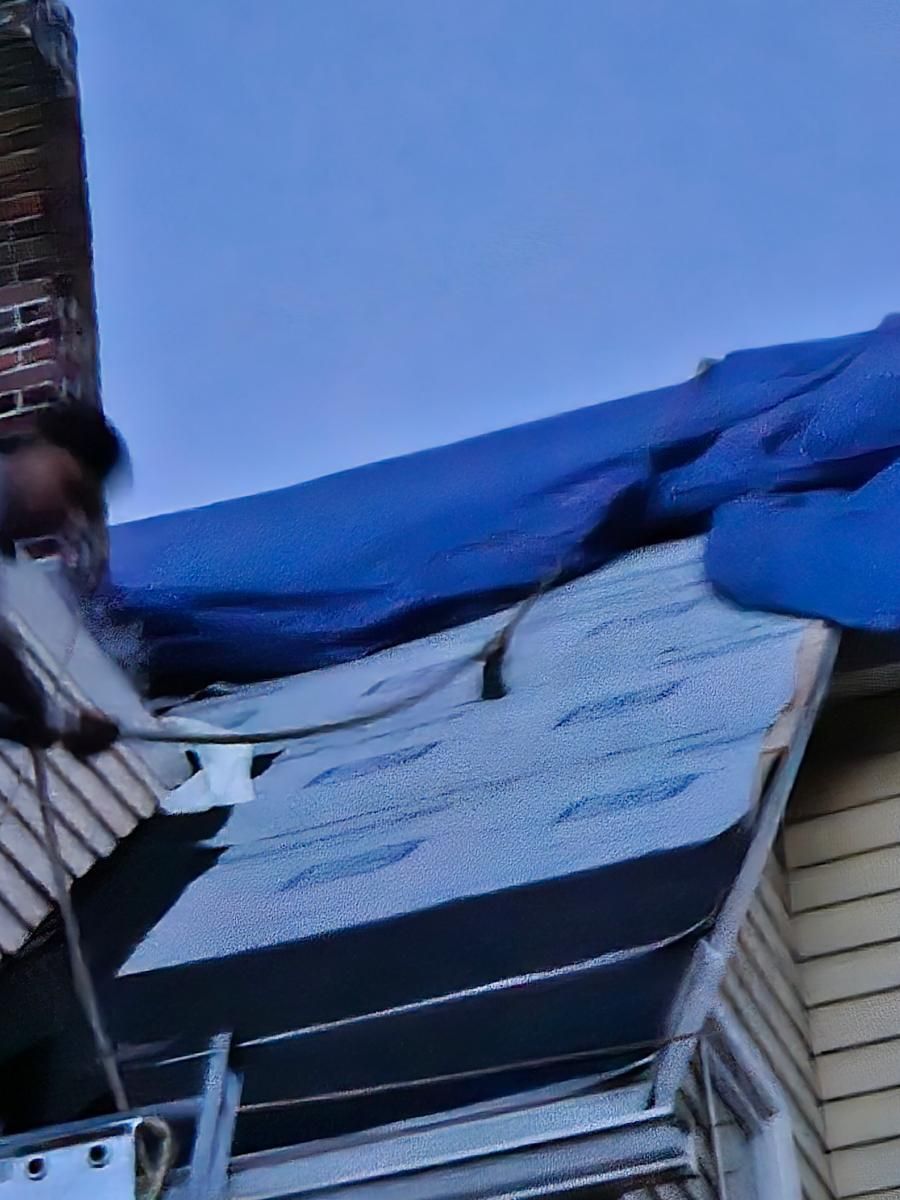 A man is working on the roof of a house with a blue tarp covering it.
