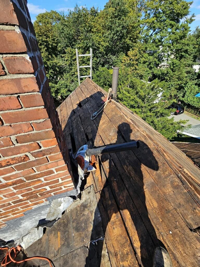 A hammer is sitting on top of a wooden roof next to a brick chimney.
