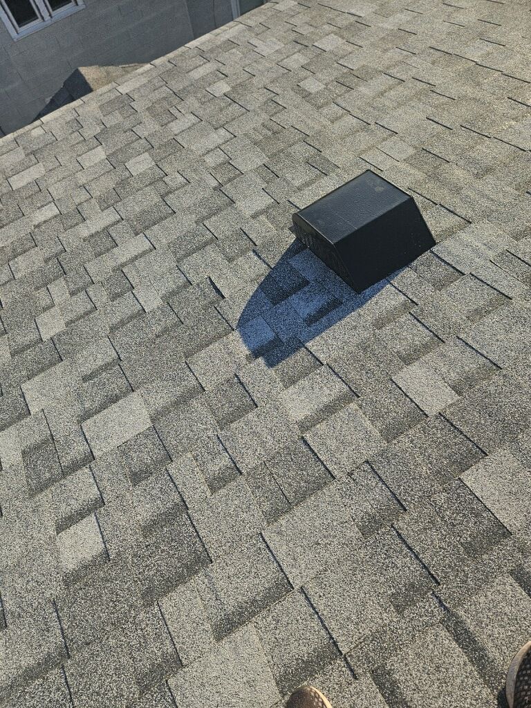 A person is standing on top of a roof with a vent on it.