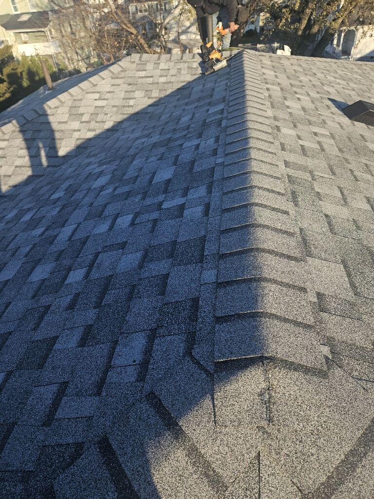 A person is standing on top of a roof with shingles on it.