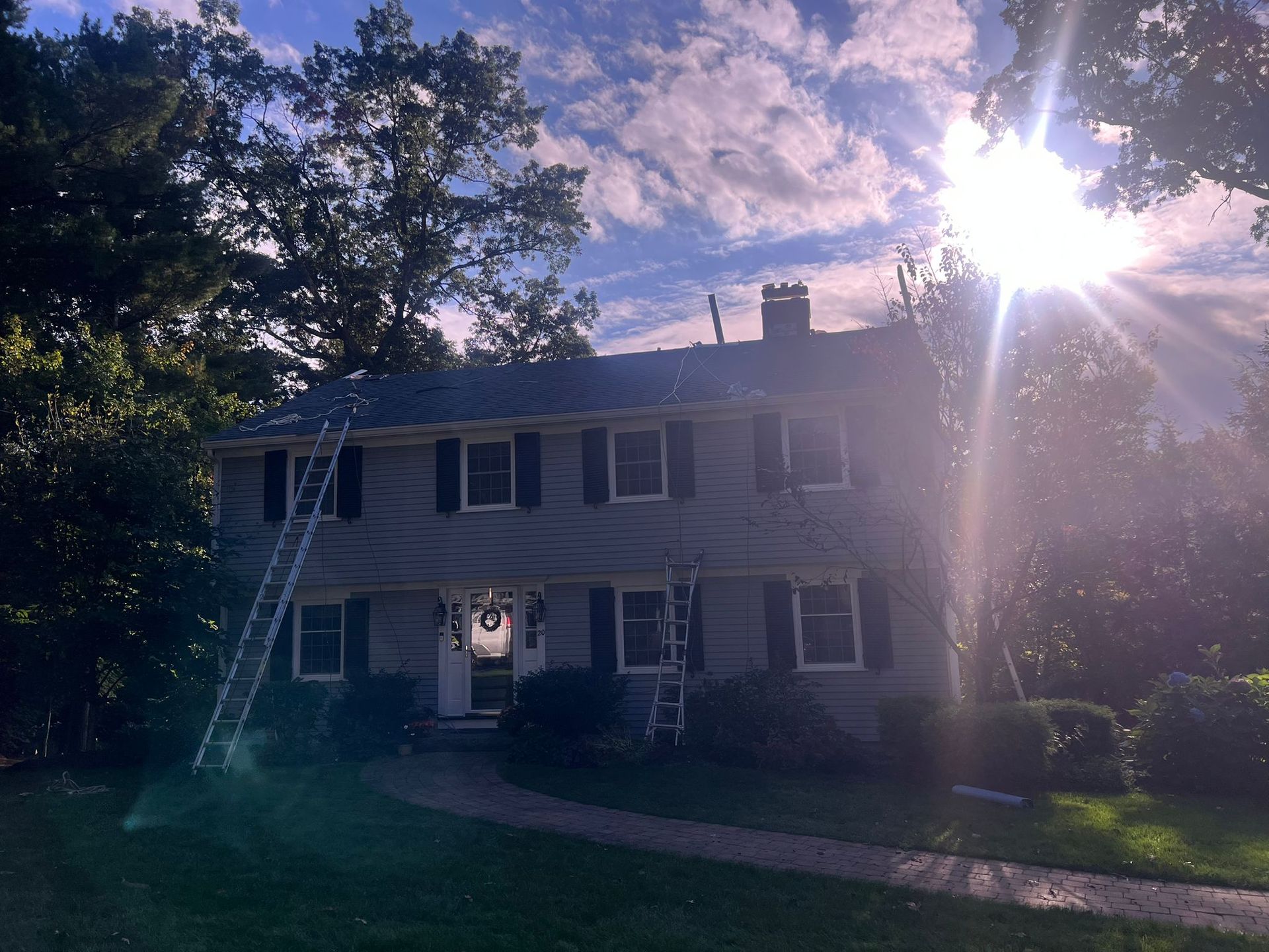 A house with a ladder in front of it and the sun shining through the trees