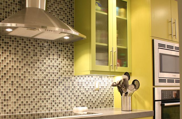 Kitchen with green cabinets, mosaic tile backsplash, stainless steel range hood, and built-in microwave.