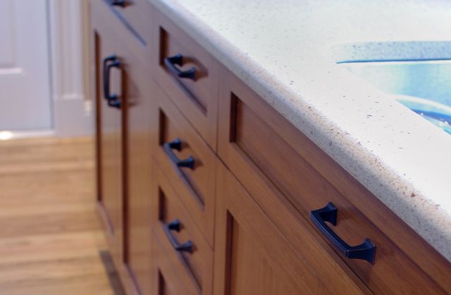Wooden kitchen cabinets with dark handles, next to a light-colored countertop.