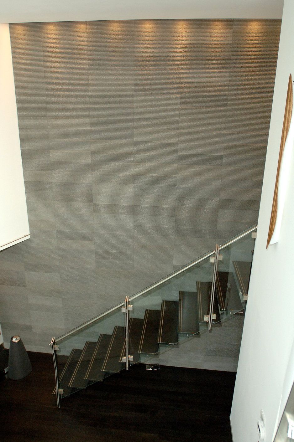 Staircase with glass railing and gray tiled wall. Dark wood flooring.