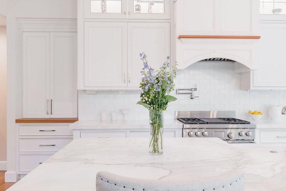White kitchen with marble island, bouquet of blue flowers, and stainless steel stove.