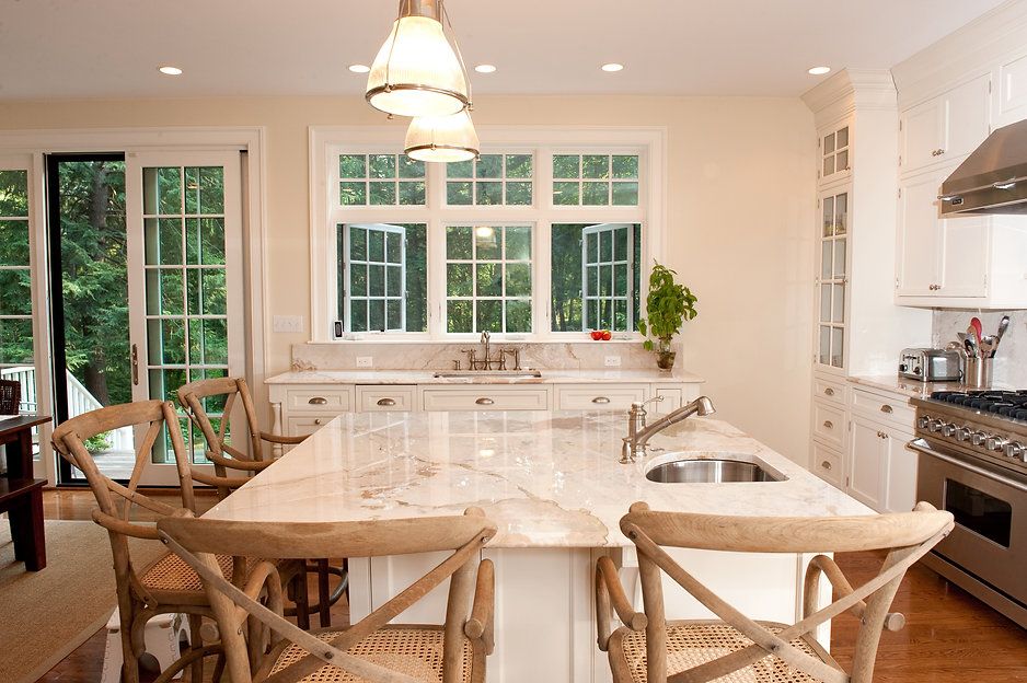 Kitchen with white cabinets, large island, and wooden chairs; windows overlook a lush green landscape.