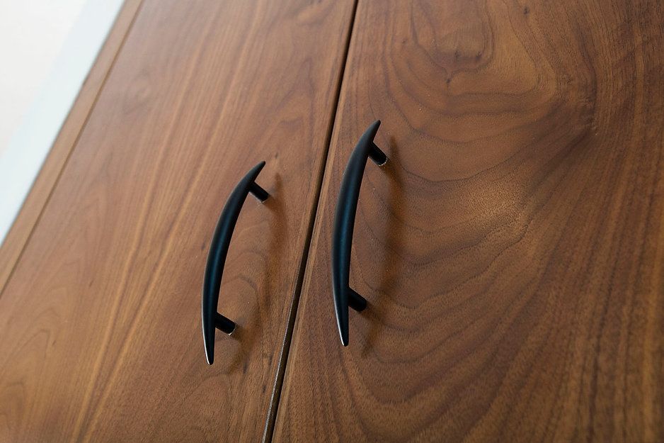 Two black arched cabinet pulls on a wooden cabinet.