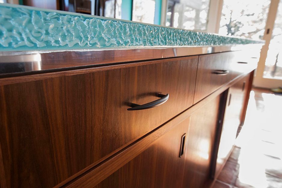 Wooden cabinets with black handles, topped by a textured, turquoise-colored countertop.