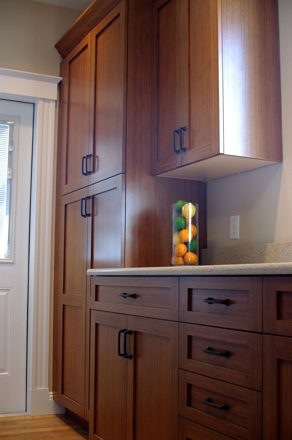 Tall wooden kitchen cabinets with dark hardware, countertop, and a jar of citrus fruits.