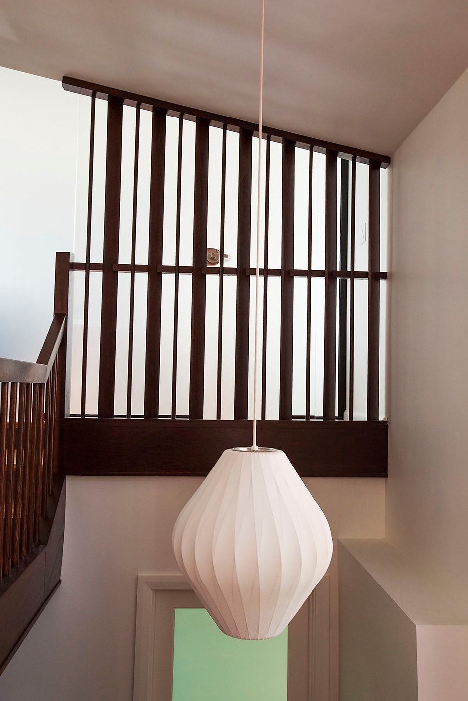 White pendant lamp hanging in stairwell with dark wood railing.