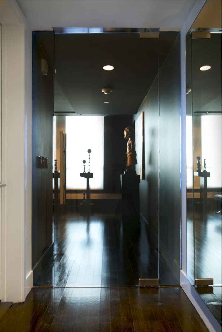 Dark hallway with mirrored walls and dark wooden floor, leading to a bright window.