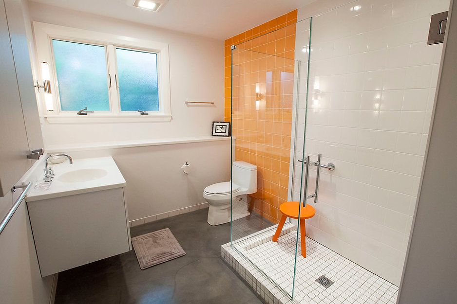 Modern bathroom with white walls, orange accent wall and stool, glass shower, and a window.