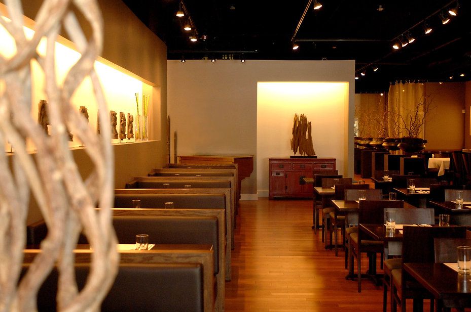 Restaurant interior with wood booths and tables, dark ceiling with spotlights, light-colored walls, and wooden floor.