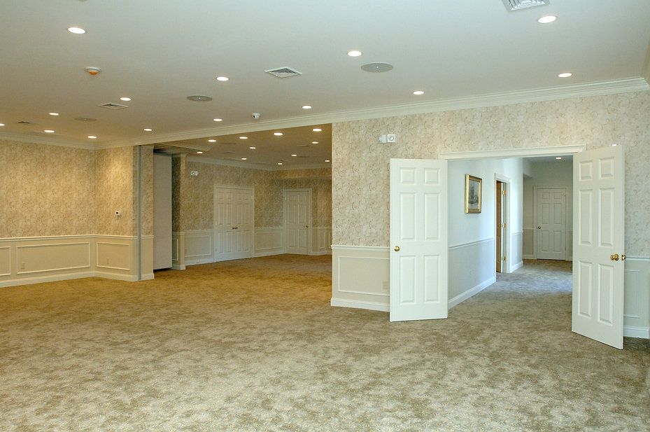 Empty room with beige carpet, white paneling, and doorways. Recessed lighting and patterned wallpaper.