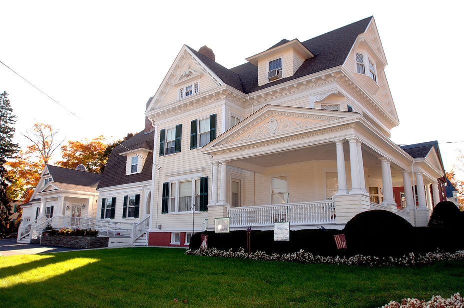 Beige Victorian house with porch and green lawn.