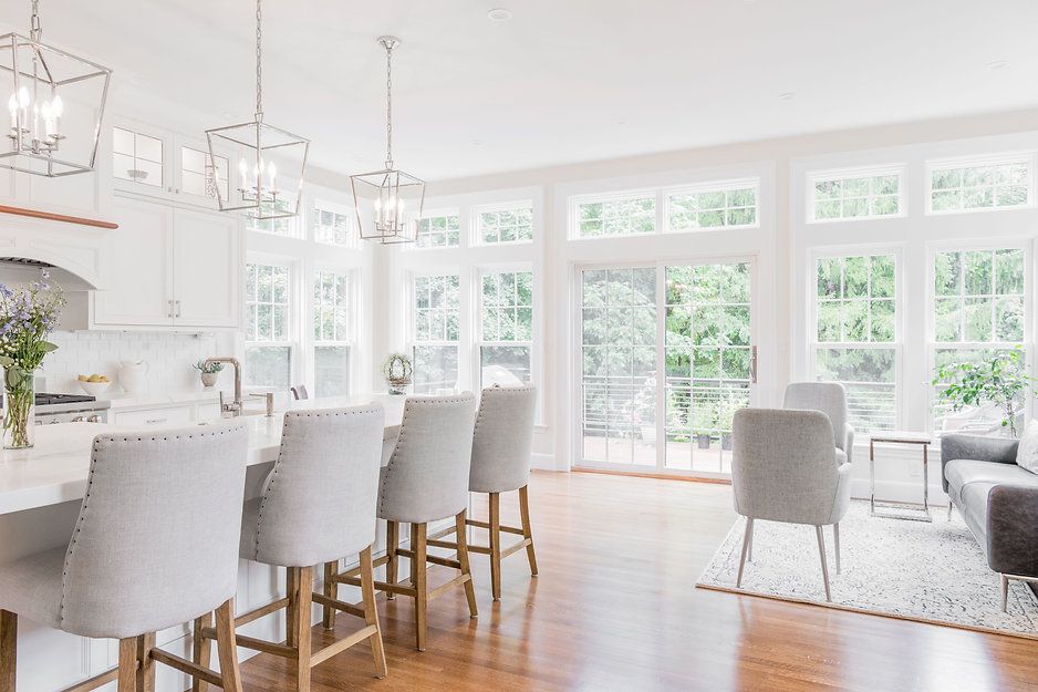 Bright white kitchen with island, bar stools, large windows, and wood floor.