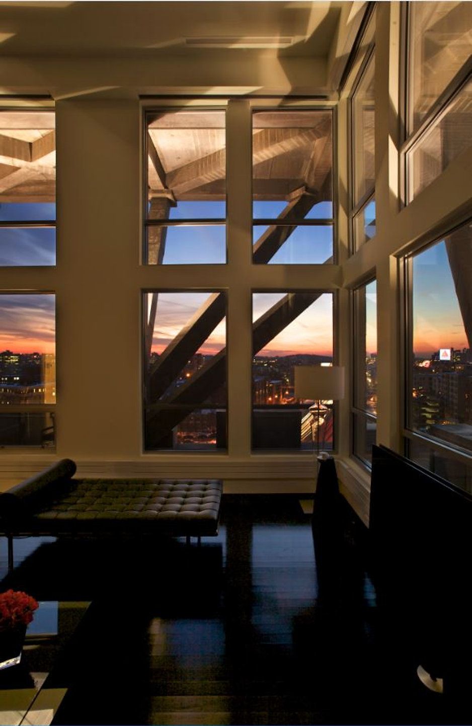 Living room with large windows showing city views at sunset, dark wood floor, black furniture.