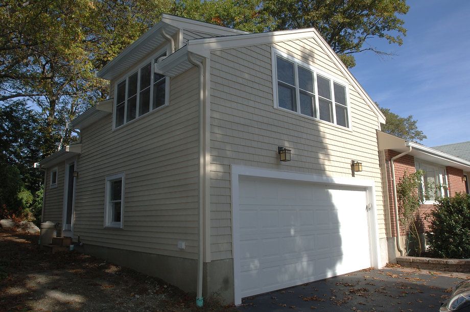 Beige two-story house with attached garage and multiple windows under a blue sky.
