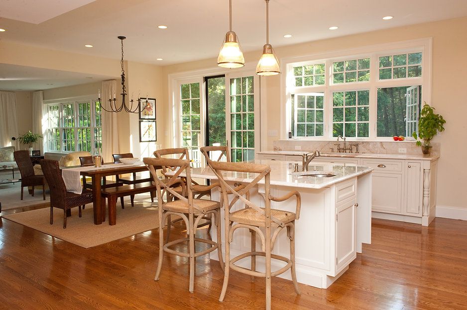 Bright kitchen with island seating, dining area, and large windows overlooking a lush green view.