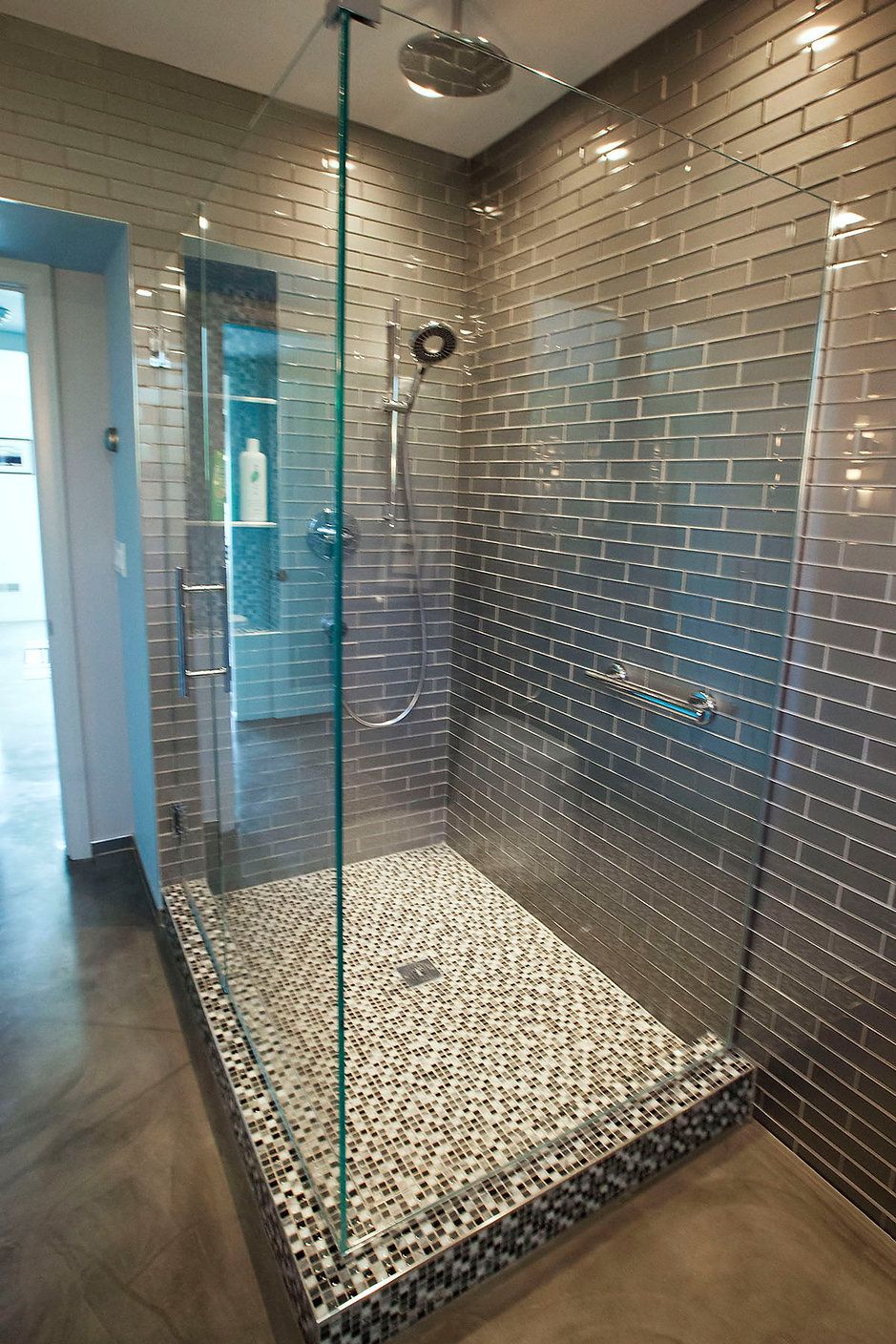 Modern shower with glass doors, pebble tile floor, and metallic brick wall.