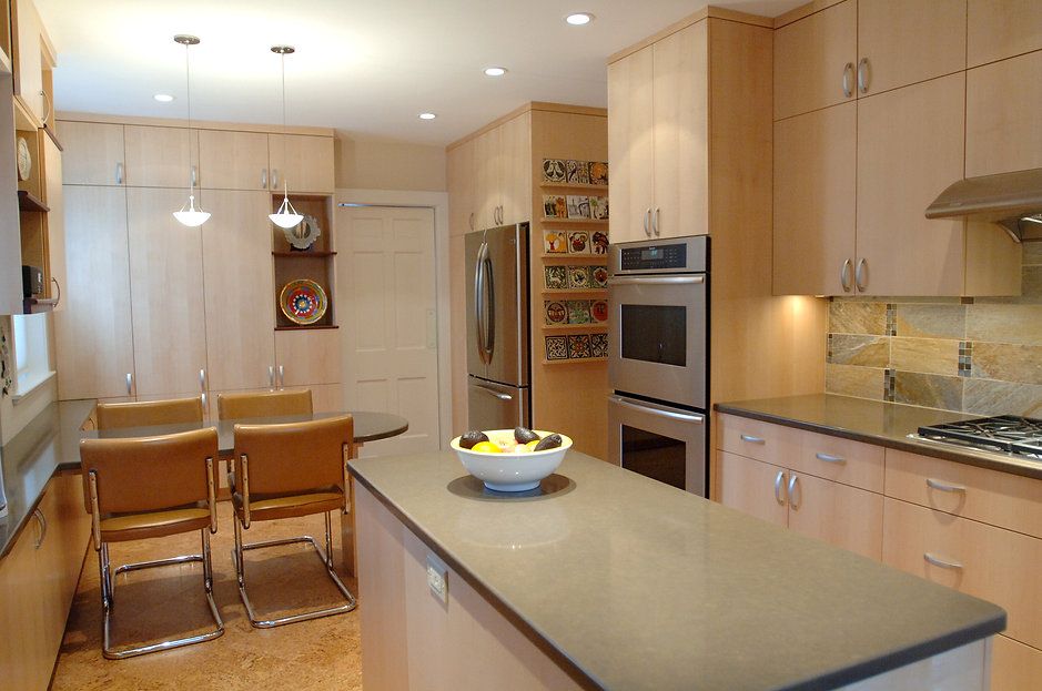 Modern kitchen with light wood cabinets, stainless steel appliances, and a gray island with a fruit bowl.