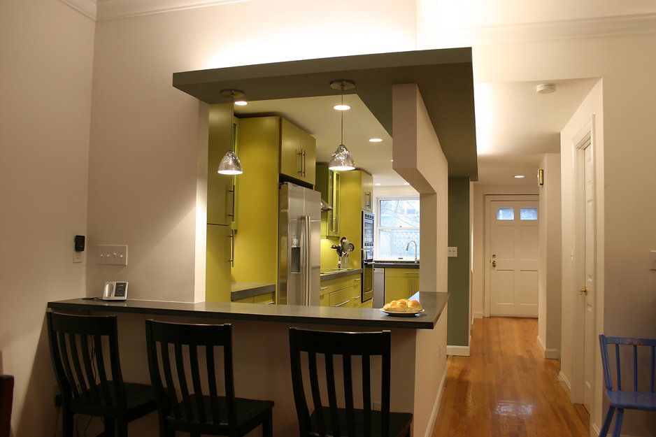 A kitchen bar with black stools, leading into a bright green kitchen.