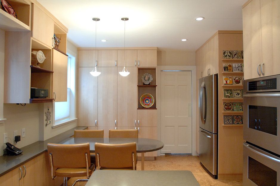 A modern kitchen with light wood cabinets, stainless steel appliances, and a small dining area.