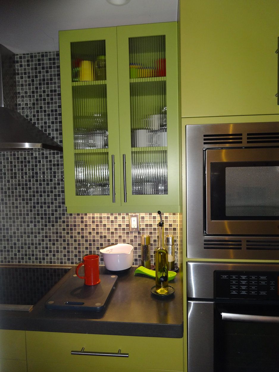 Lime green kitchen cabinets with a built-in microwave, above a black countertop with a red pitcher and a white bowl.