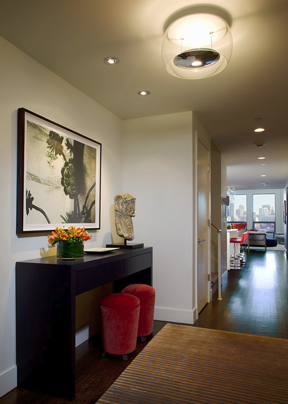 Hallway with dark console table, artwork, red stools, and modern light fixture.