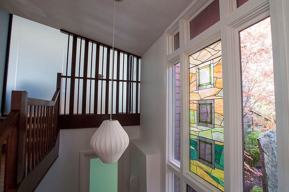 Staircase with wooden railing, white walls, and a large window with a stained glass panel showing a building.