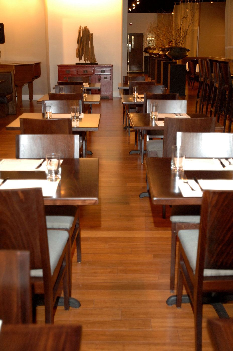 Empty restaurant interior with rows of wooden tables and chairs, brown flooring.
